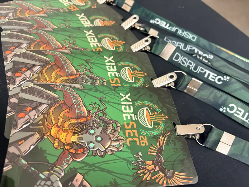 Crachás do XibéSec 2026 com a arte do mascote e os cordões da Disruptec, separados para o credenciamento.