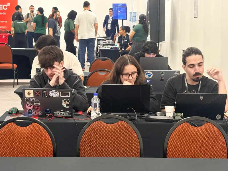 Participantes concentrados nos notebooks, numa mesa da área do evento.